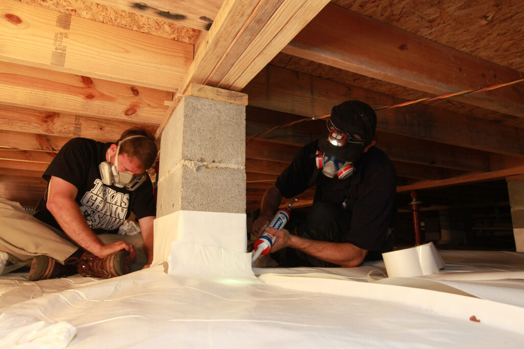 Workers sealing crawl space with caulk and vapor barrier