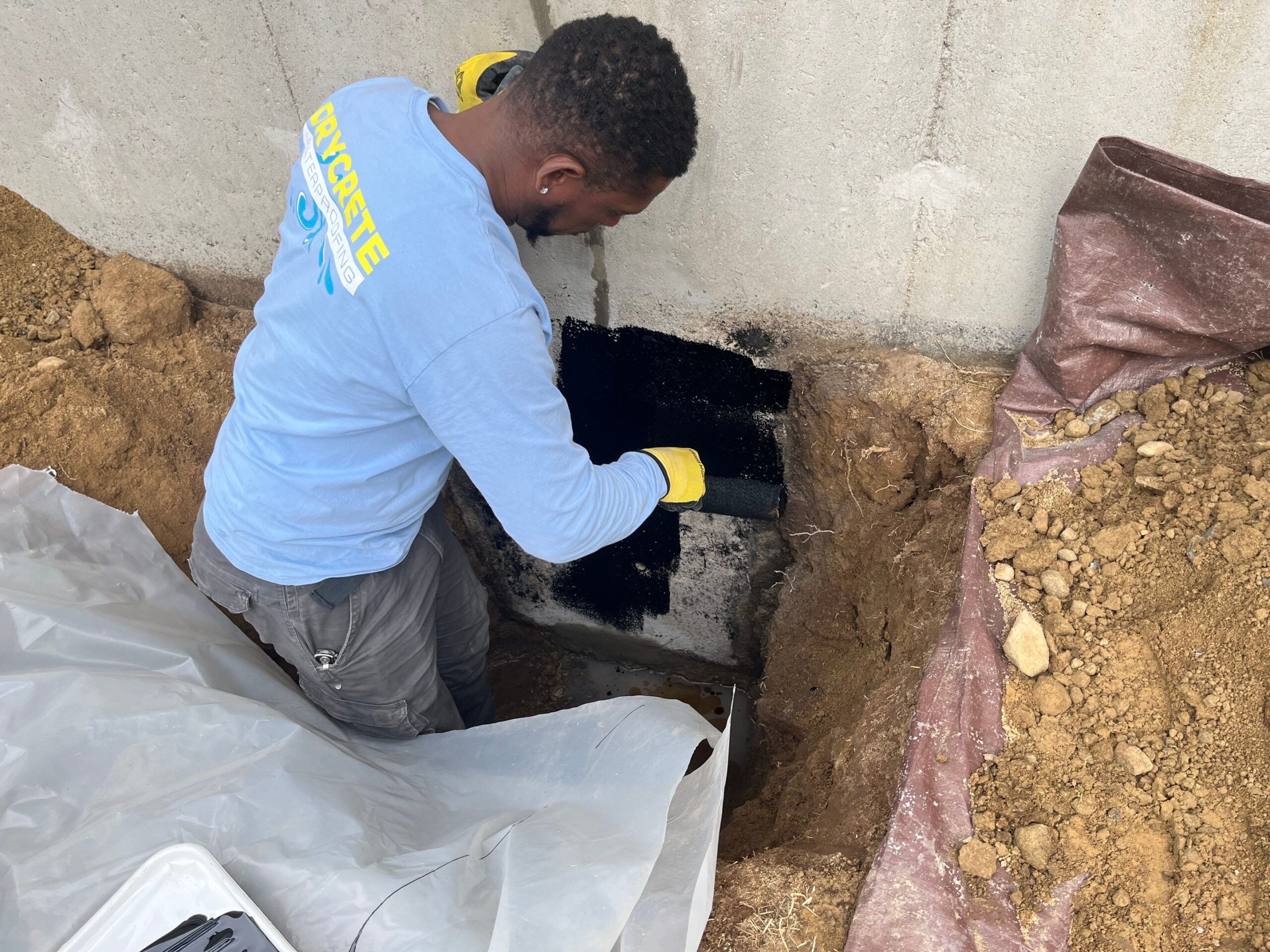 Restore Your Home's Foundation Crack Repair 2 Worker applying waterproofing material to the exterior foundation wall of a house.