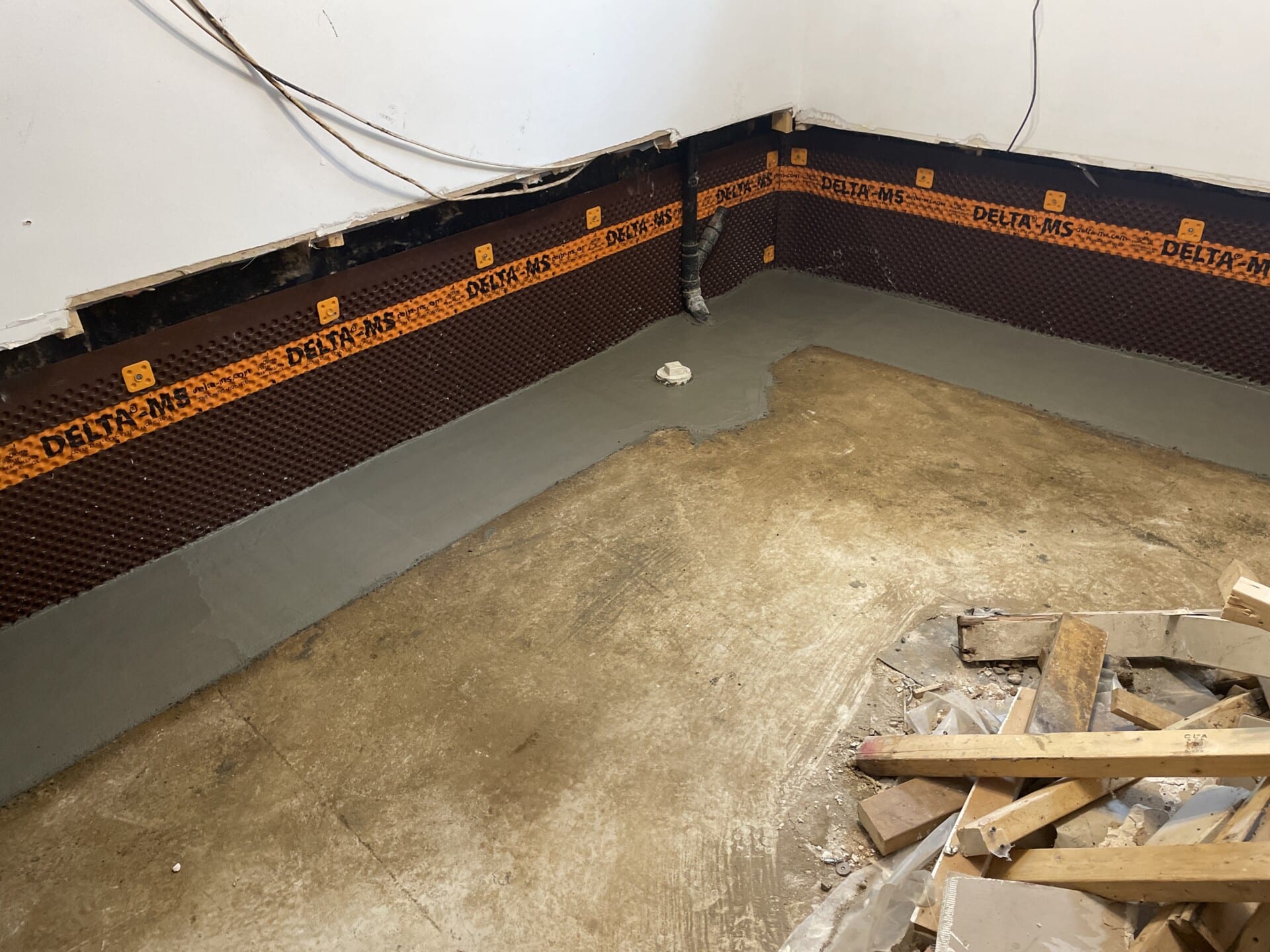 Our Professional Basement Waterproofing Experts Can Help 1 Construction site floor with black/orange waterproofing, materials scattered.
