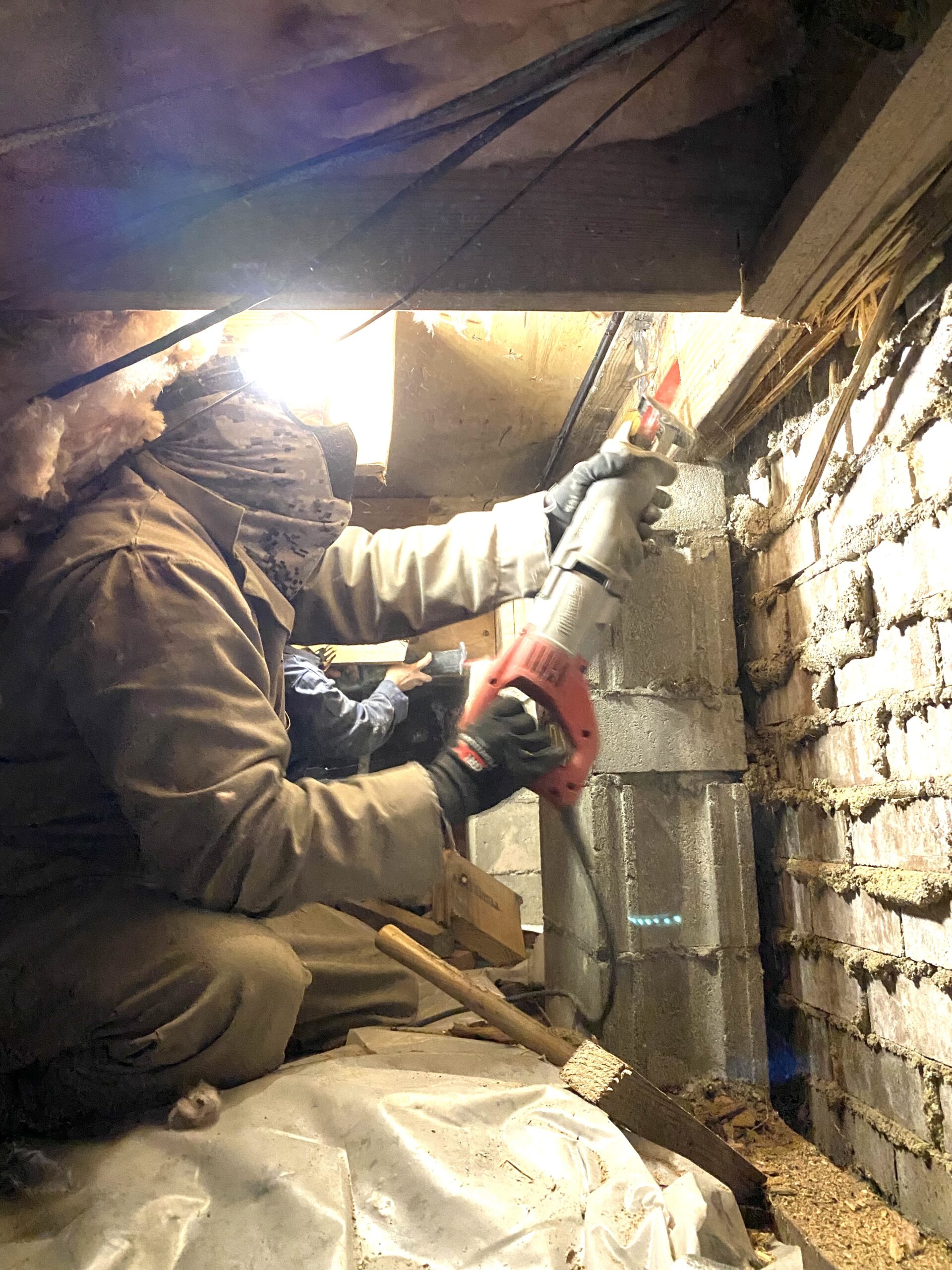 Technician repairing crawl space foundation with power tool.