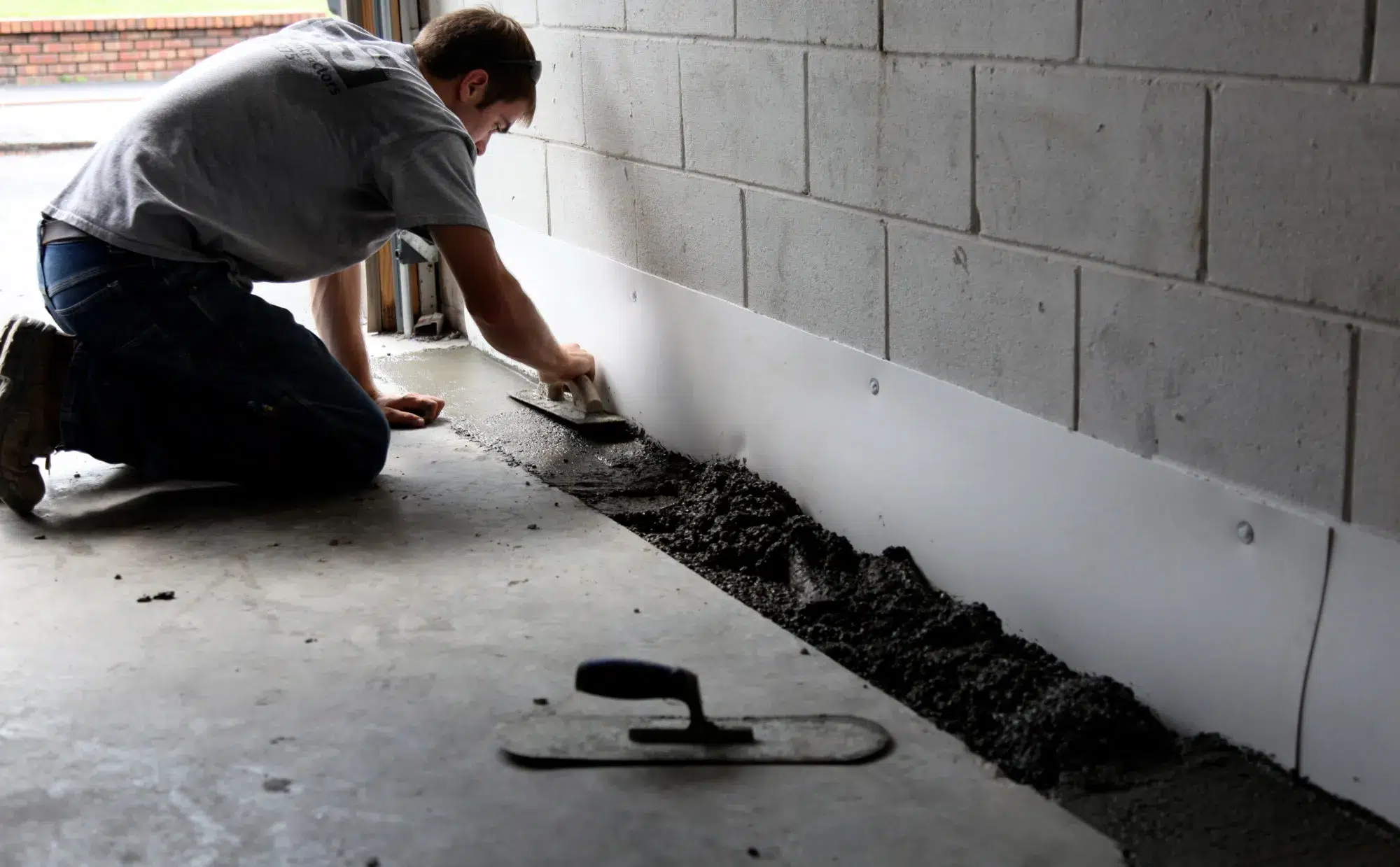 Worker installing basement waterproofing system with fresh concrete