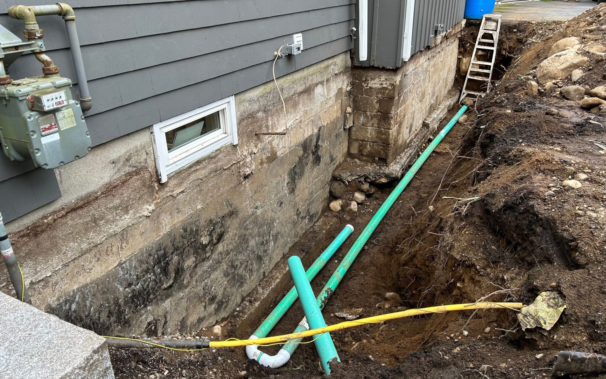 Water Runoff Solutions in DC, MD, VA - Our Services 2 A view of a house foundation with exposed green drainage pipes and a nearby ladder.