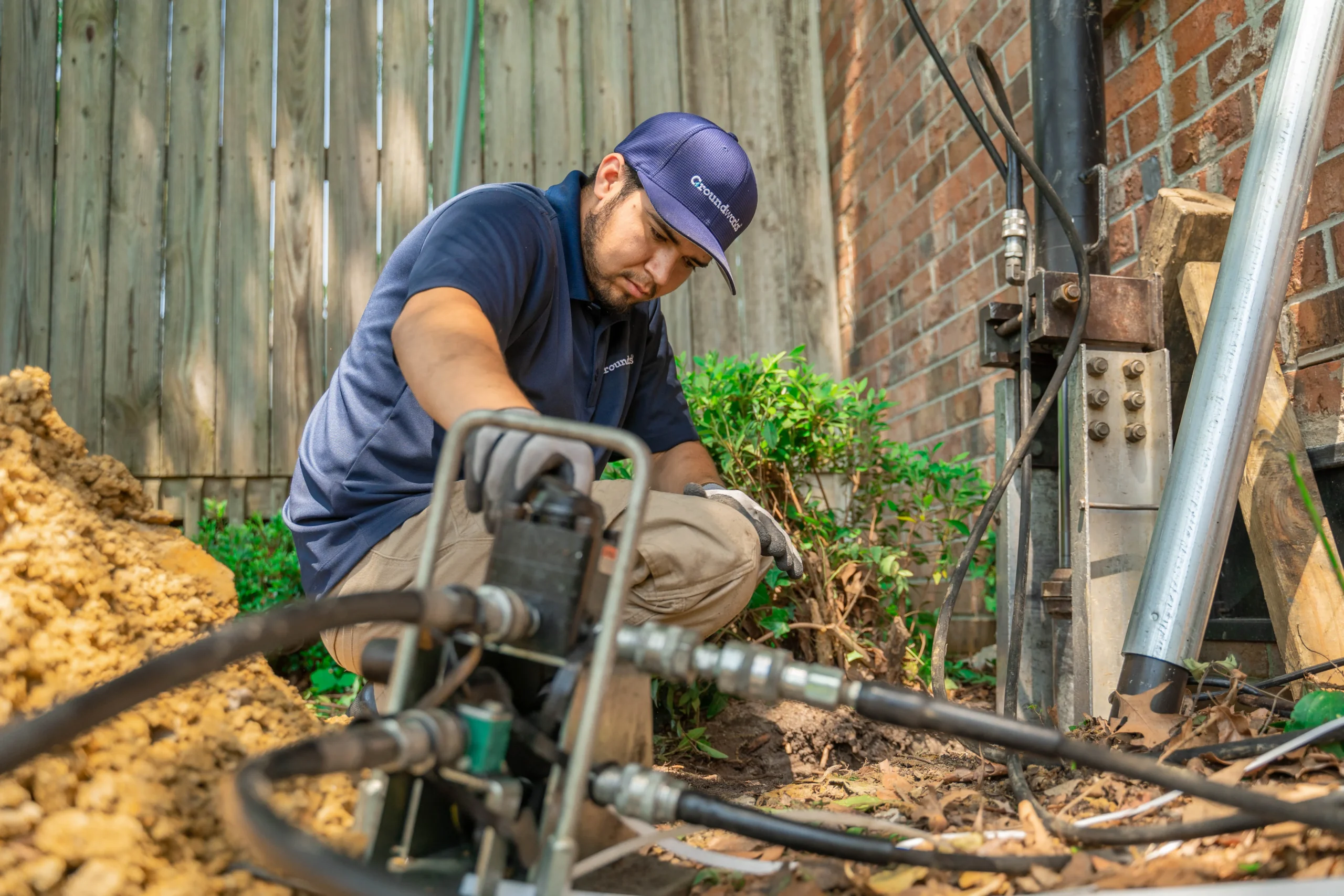 Soggy Ground Repair Services by Us - DMV Area 1 : A worker performing foundation repair, using equipment near a brick wall in a backyard.