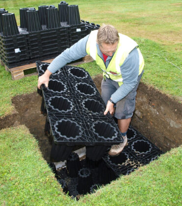 Worker installing drainage soakaway system in a trench with modular plastic drainage blocks.