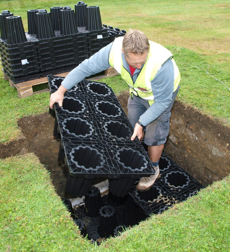 Worker installing drainage soakaway system in a trench with modular plastic drainage blocks.