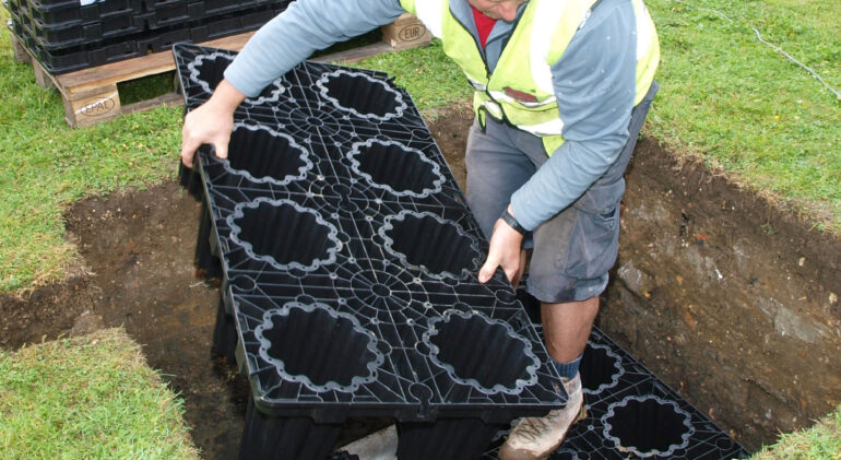 Worker installing drainage soakaway system in a trench with modular plastic drainage blocks.