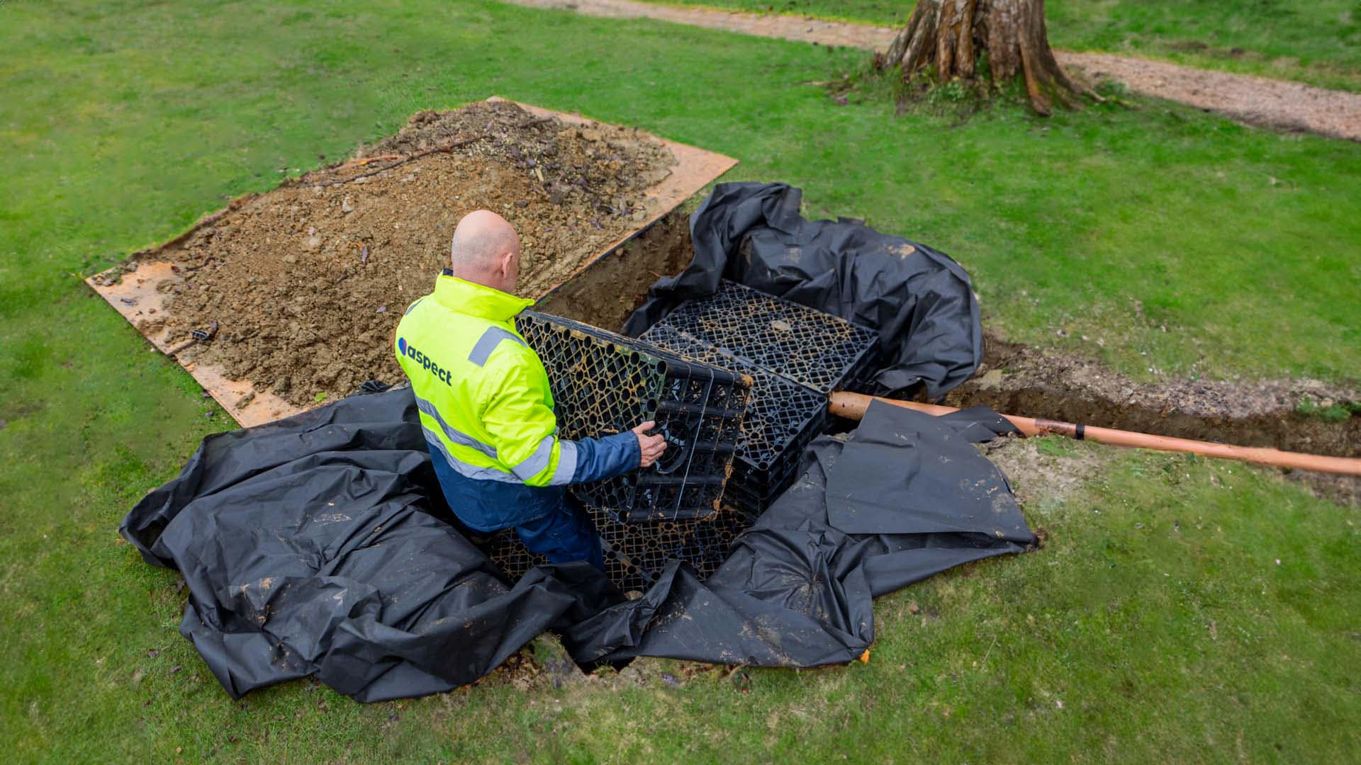 We Design Stormwater Management Systems Across the US 2 A worker installing a drainage soakaway system in a trench, wearing a high-visibility jacket.