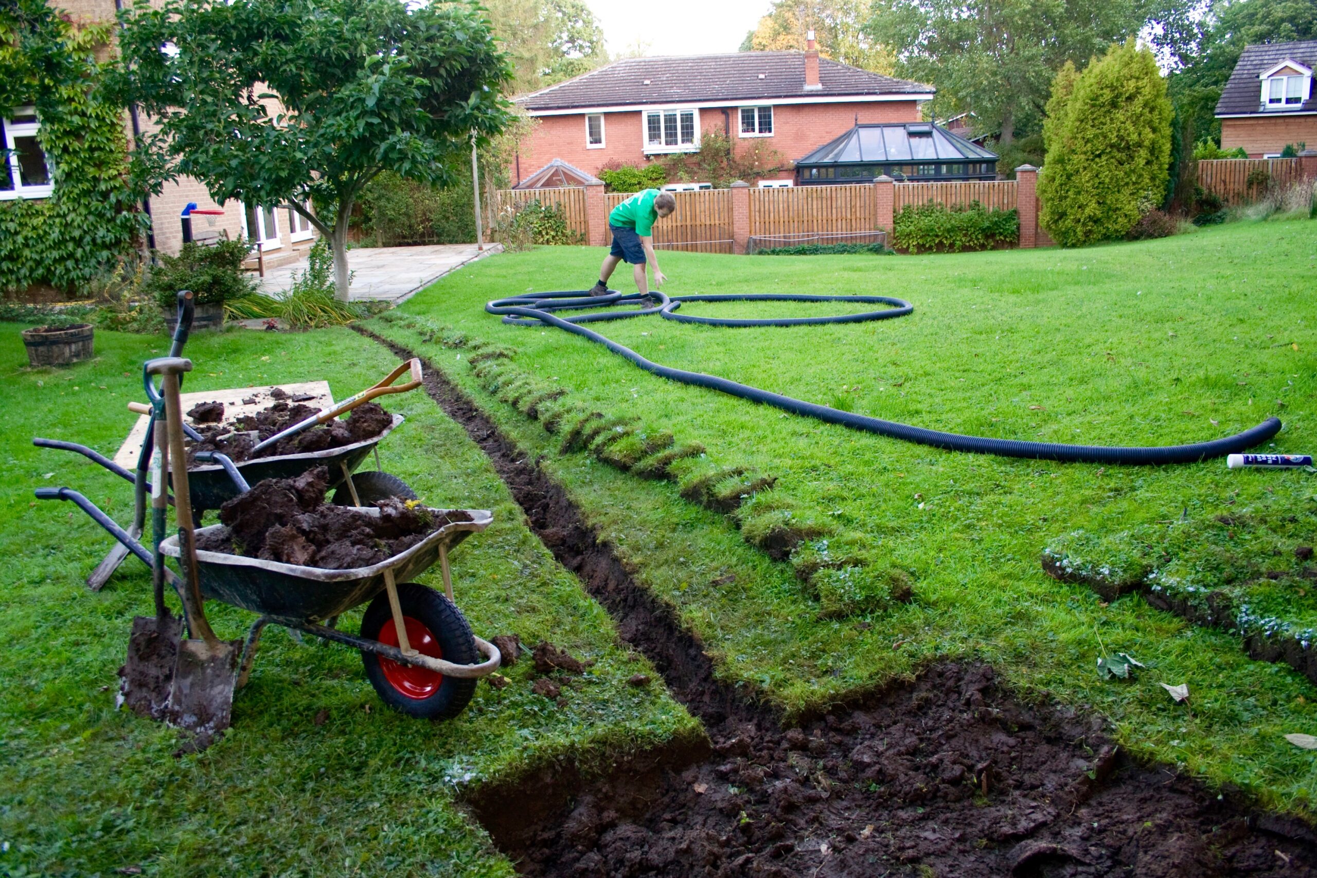 We Design Stormwater Management Systems Across the US 1 A worker is laying drainage pipes in a garden, preparing for a garden drainage installation.