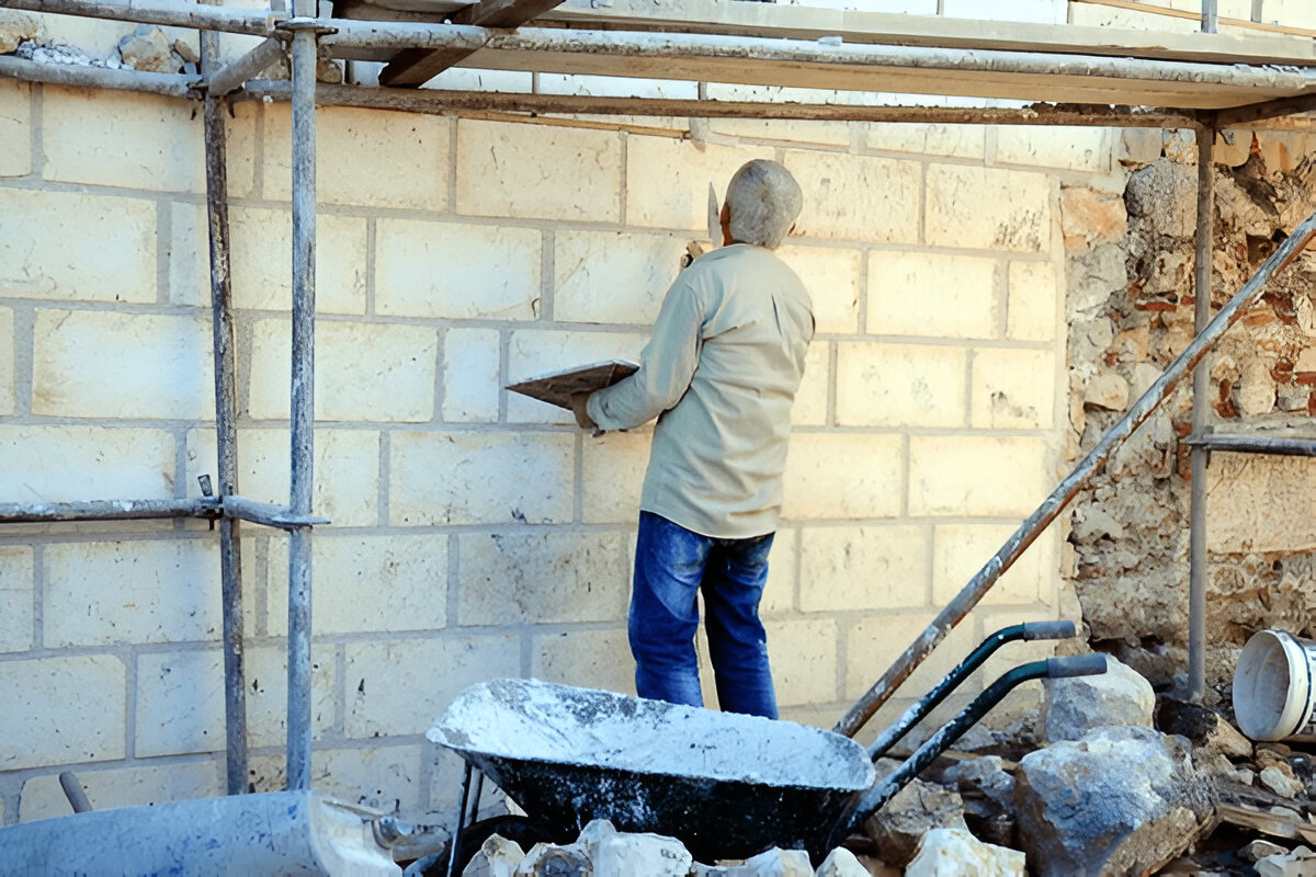 Construction worker applying plaster on exterior brick wall for waterproofing.