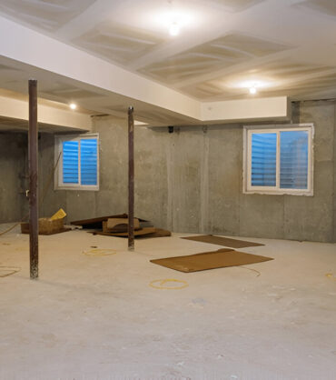 An unfinished basement with concrete walls, support beams, and exposed construction materials.