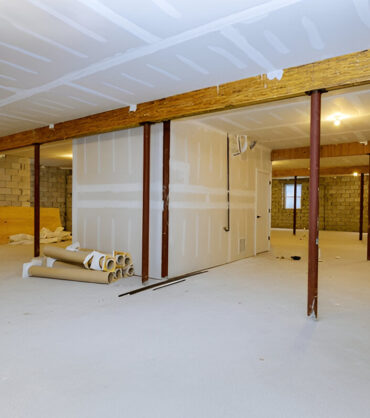 An unfinished basement with drywall installation in progress and exposed concrete block walls.