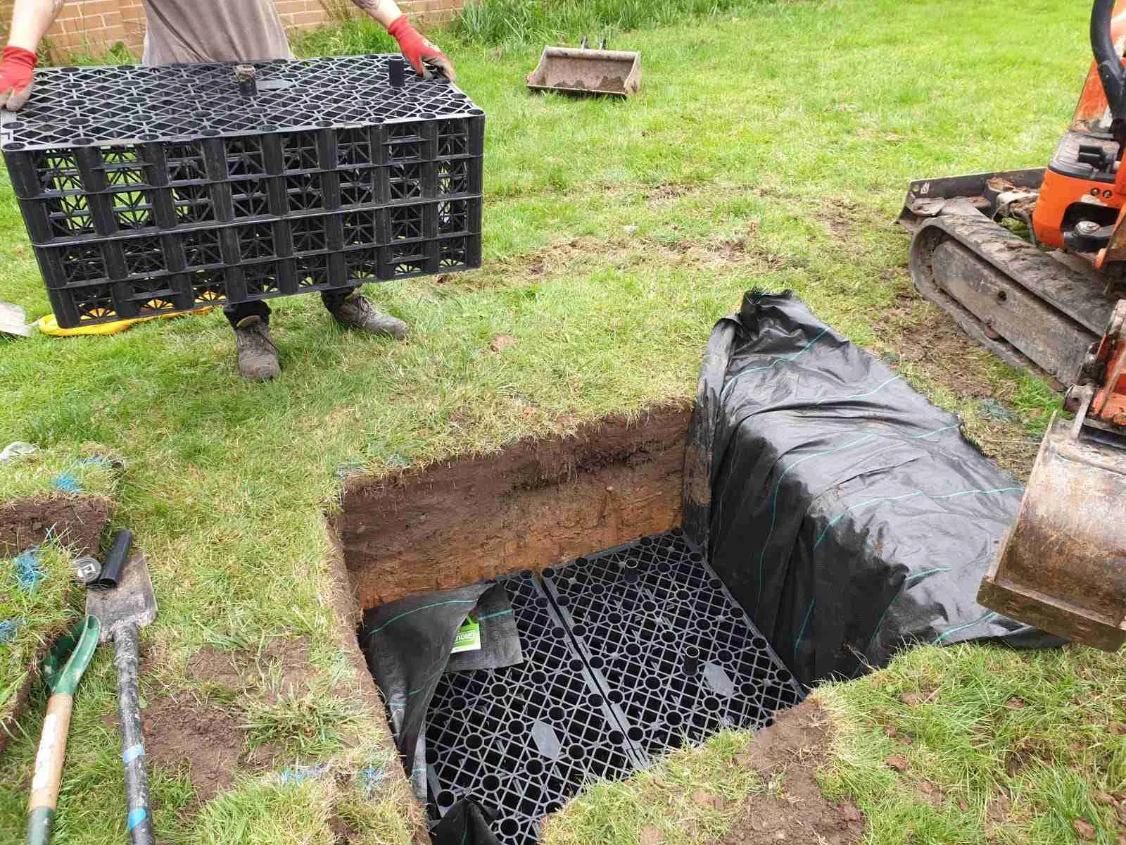 Installation of a soakaway crate system being placed into a prepared trench in a garden.