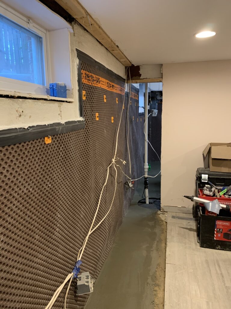 Construction site floor with black/orange waterproofing, materials scattered.