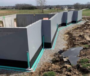 A newly constructed foundation with waterproofing pipes and gravel surrounding it.