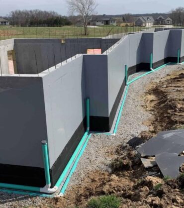 A newly constructed foundation with waterproofing pipes and gravel surrounding it.