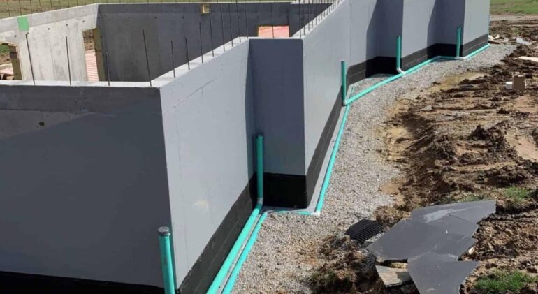 A newly constructed foundation with waterproofing pipes and gravel surrounding it.