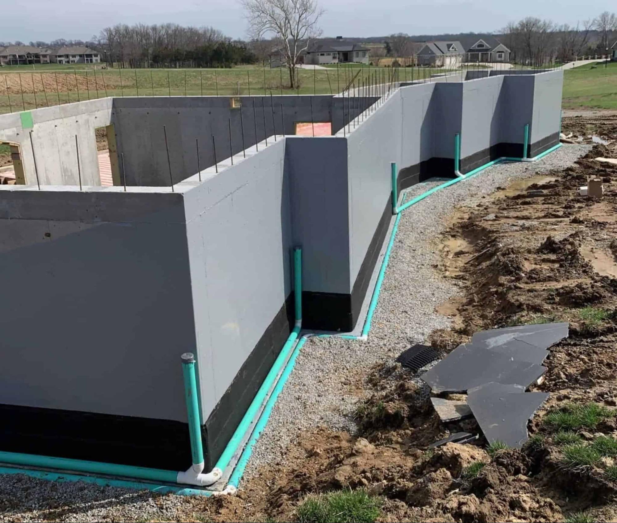 A newly constructed foundation with waterproofing pipes and gravel surrounding it.
