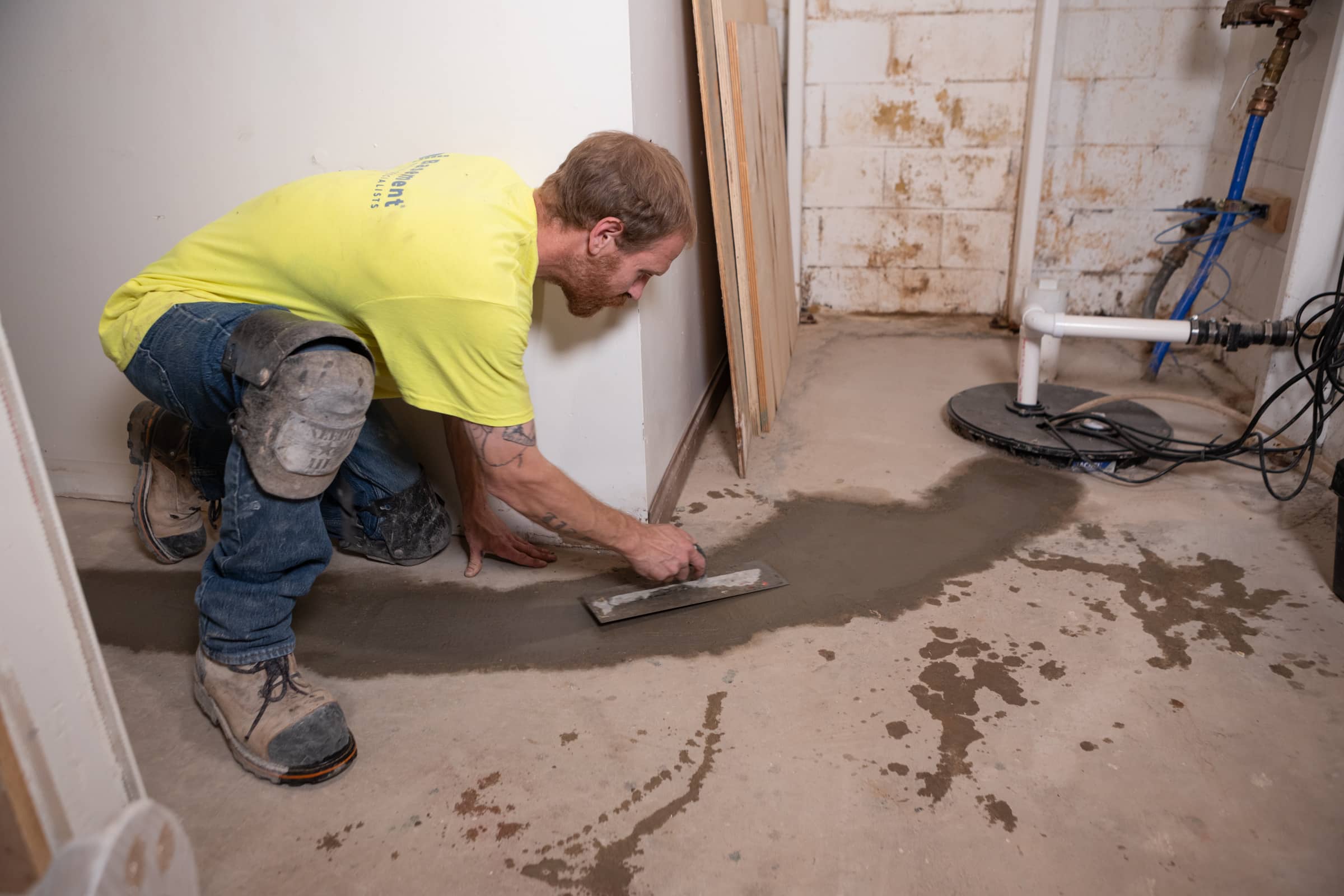 Worker sealing basement floor with concrete near a sump pump system