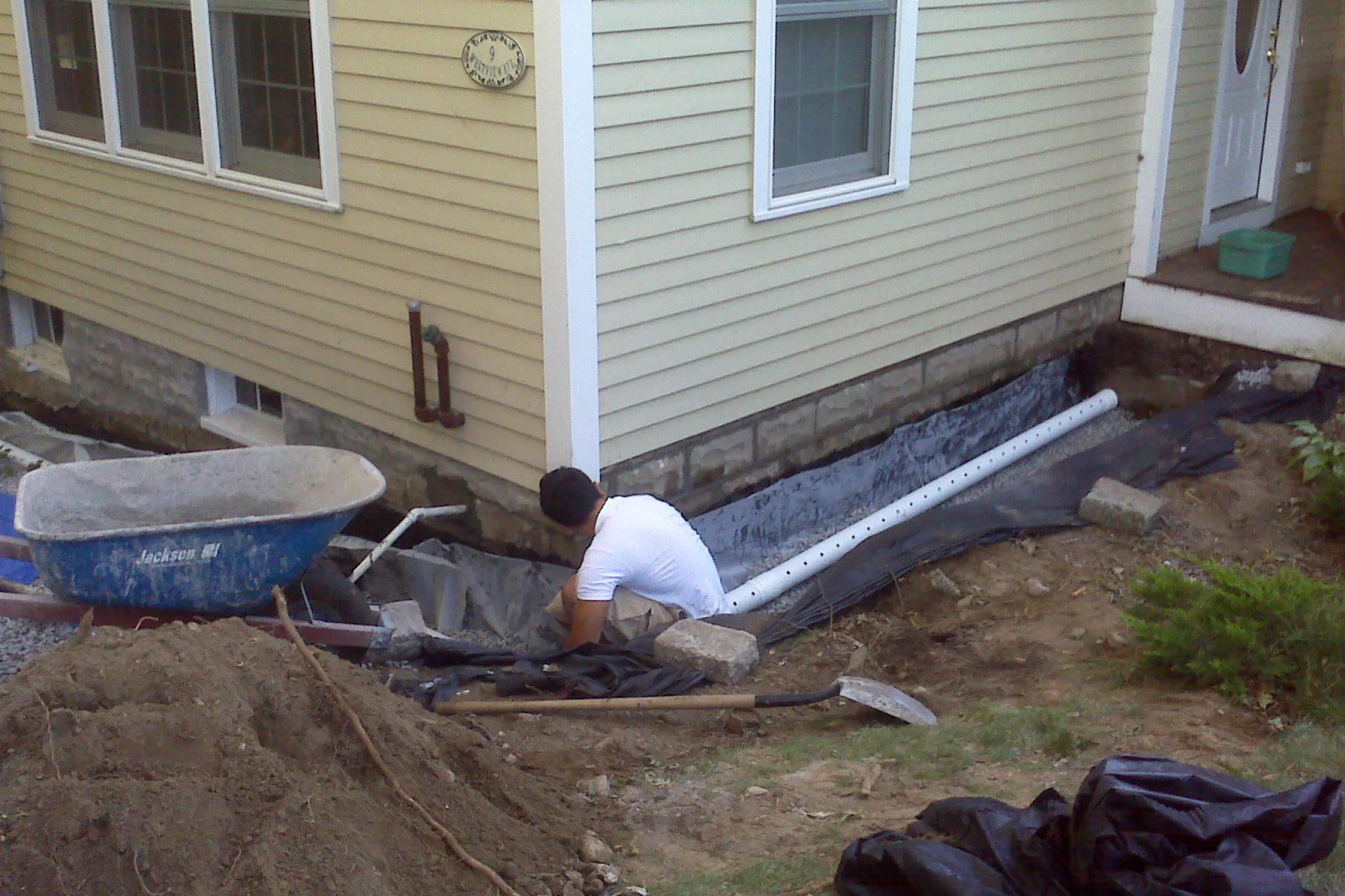 Worker installing a French drain system along the foundation of a house.