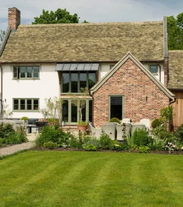 Traditional country-style house with a brick and wood exterior, surrounded by a landscaped garden and green lawn.