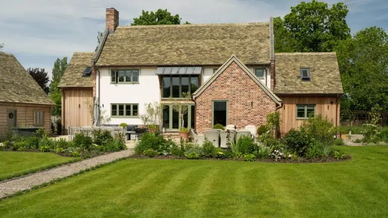 Traditional country-style house with a brick and wood exterior, surrounded by a landscaped garden and green lawn.