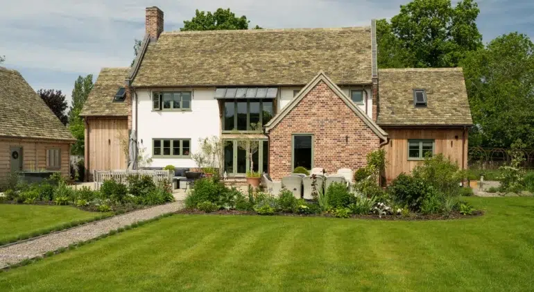 Traditional country-style house with a brick and wood exterior, surrounded by a landscaped garden and green lawn.