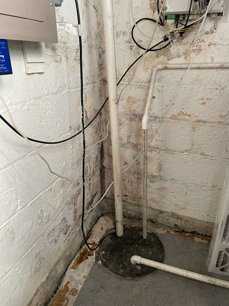Before — the home's old corner sump pit beside a mold- and efflorescence-stained concrete-block basement wall