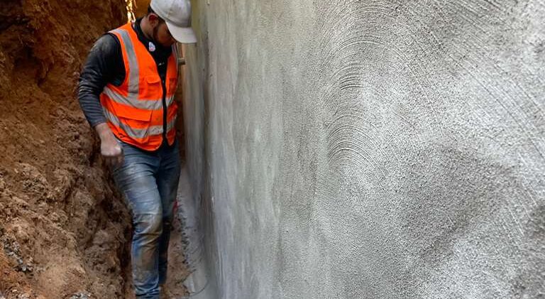Water on Three Sides: Sealing a 1940s Block Home From the Outside on Massachusetts Ave 5 A DMV Waterproofing crew member in the excavated trench beside a foundation wall sealed with a cementitious waterproofing coat in Bethesda, MD