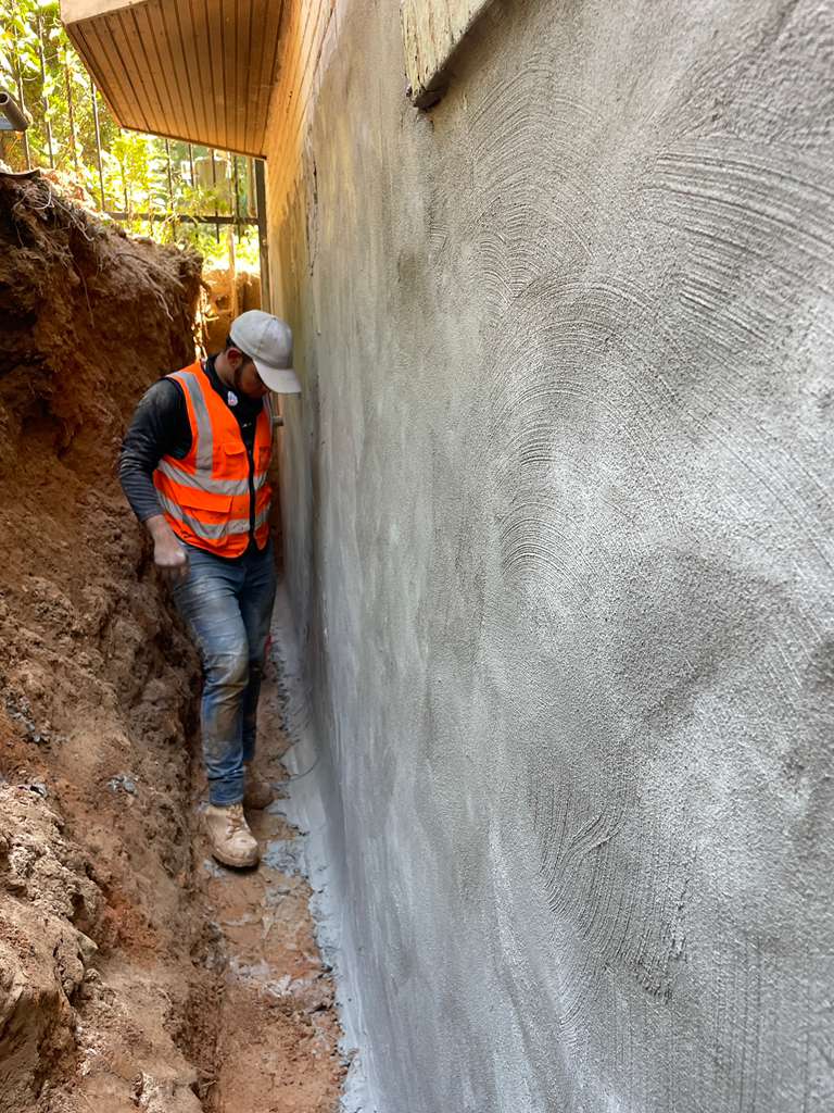 A DMV Waterproofing crew member in the excavated trench beside a foundation wall sealed with a cementitious waterproofing coat in Bethesda, MD