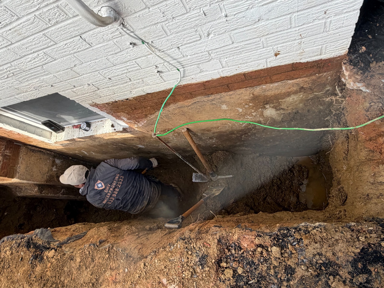 DMV Waterproofing crew member excavating along the brick foundation to the footing