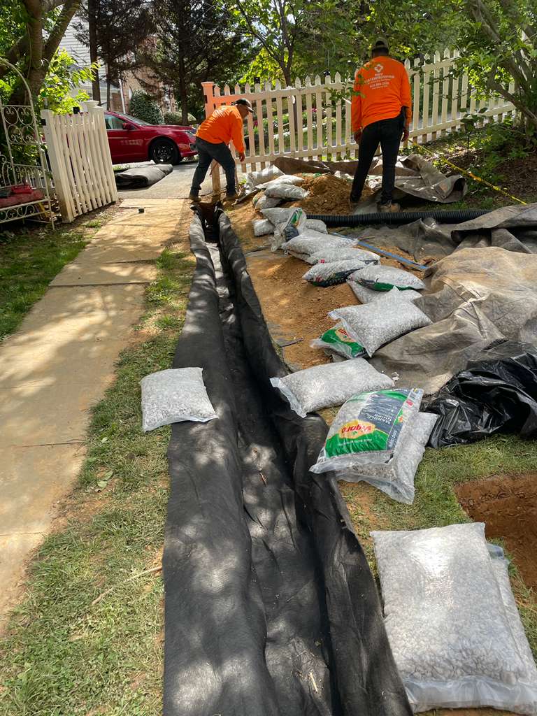 DMV Waterproofing crew staging bags of washed stone along the open trench — North Potomac, MD