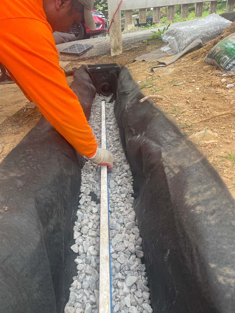 Straightedge laid along the stone bed to verify consistent fall before the pipe goes in — North Potomac, MD
