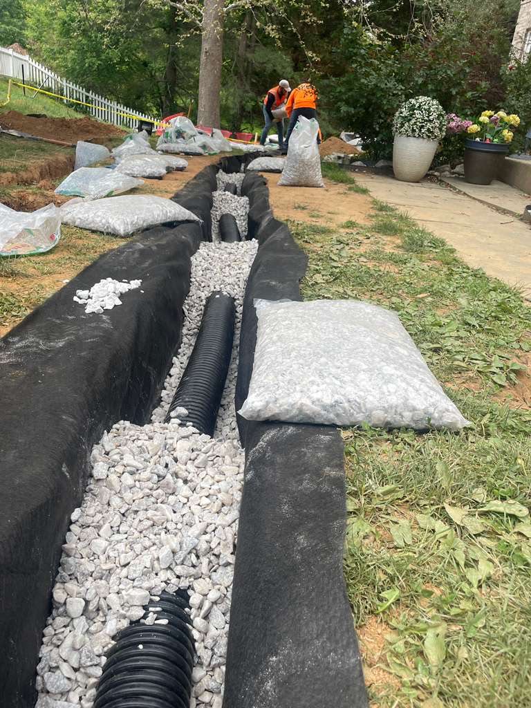 Six-inch perforated pipe bedded in #57 washed stone inside the geotextile wrap — North Potomac, MD