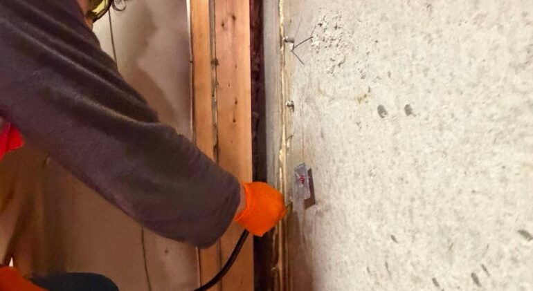 Injection hose connected to a packer in a concrete foundation wall, with cured grout visible along the crack above it