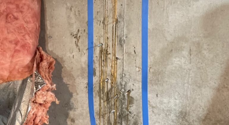 A vertical row of injection packers set into a poured concrete foundation wall, with polyurethane grout bleeding out along the line of the crack