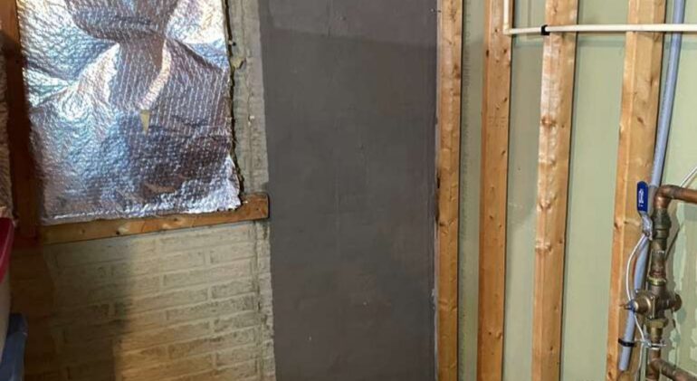 Basement wall with a smooth grey cementitious strip covering a repaired foundation crack, framing and insulation alongside