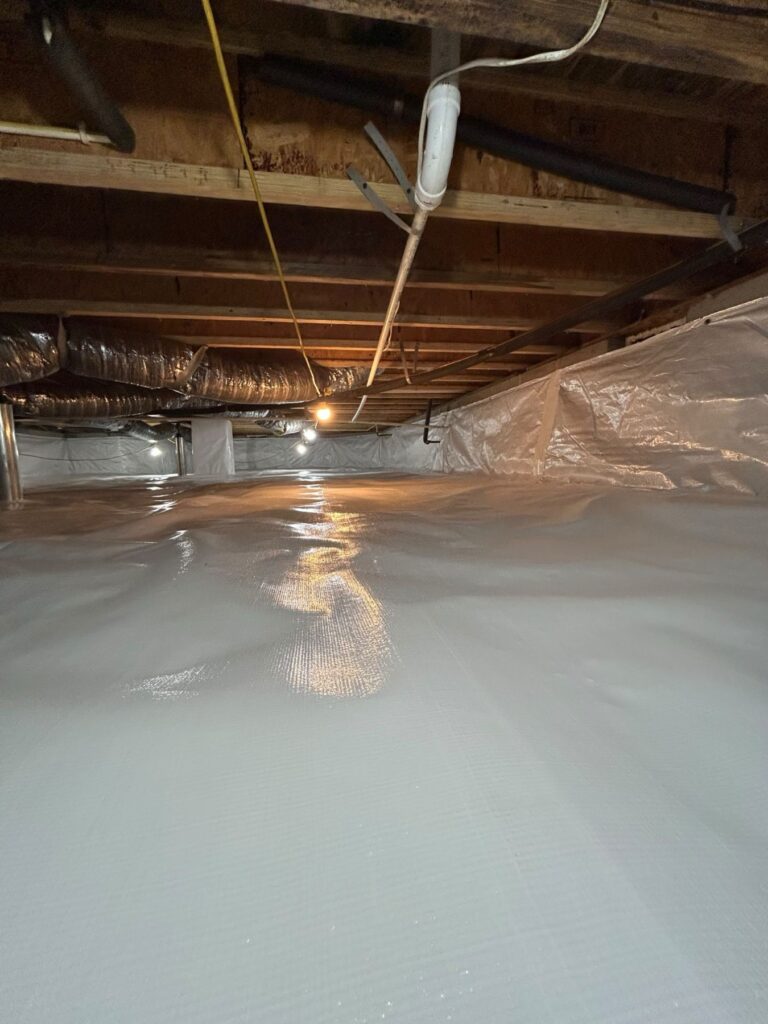 White ground liner spanning a crawl space floor beneath overhead ducts and exposed joists