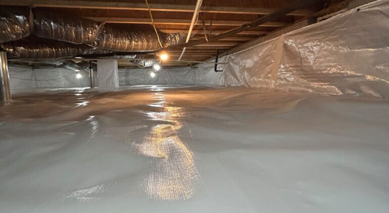 Wide view of a completed crawl space encapsulation, the sealed floor barrier running the full width beneath insulated ducts