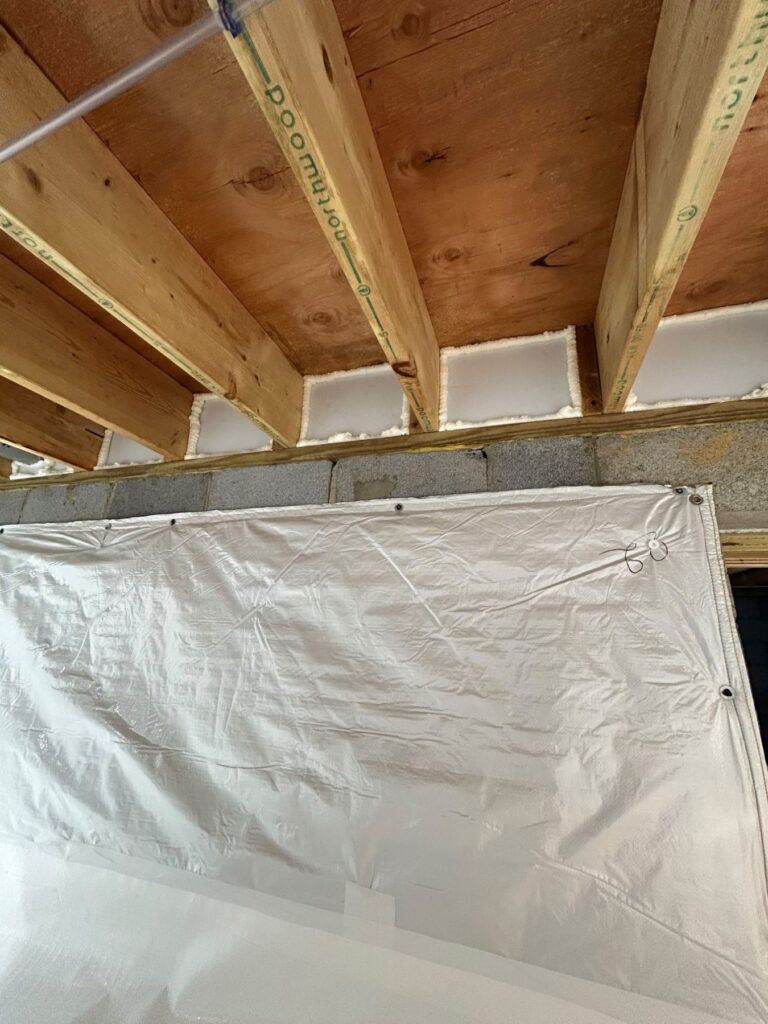 Rim joist pockets sealed with sprayed foam between the floor joists above a crawl space foundation wall