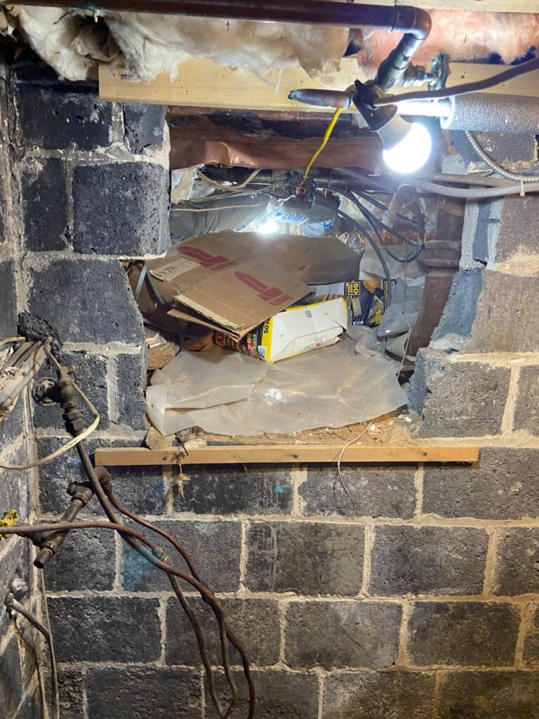 Large unsealed opening in a crawl space block wall packed with cardboard and loose plastic