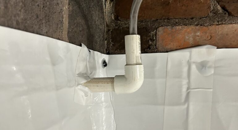 The Crawl Space That Was Cooling the Whole House: A Bethesda Encapsulation 4 Sealed white vapor barrier mechanically fastened to a crawl space foundation wall, with a condensate discharge line routed through it and out through the wall