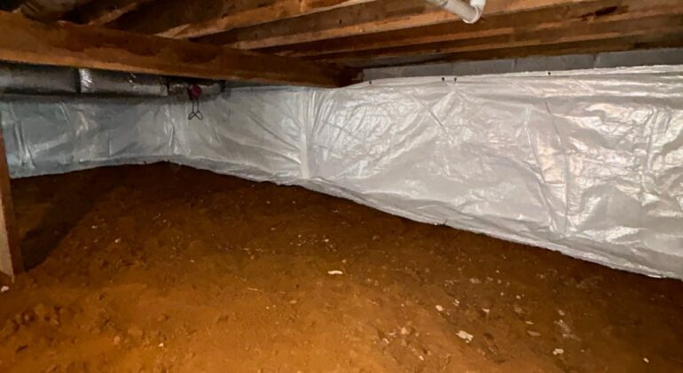 Crawl space with a sealed white liner fastened to the foundation wall and the dirt floor deliberately left uncovered