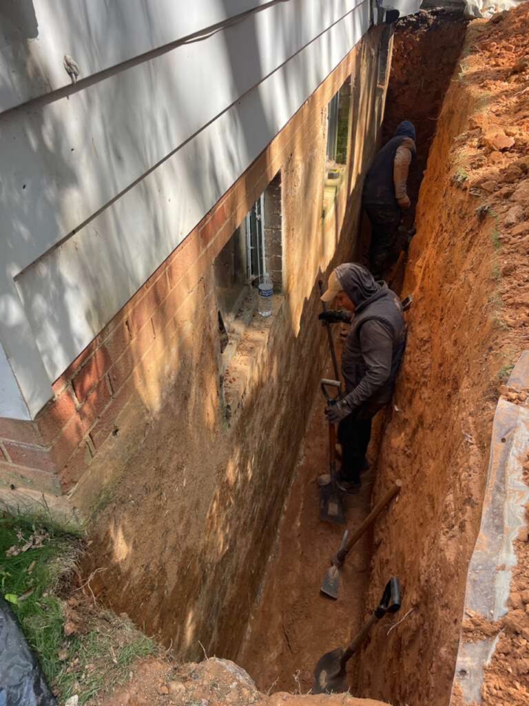 Crew digging an exterior trench down to the footer alongside a brick and block foundation wall