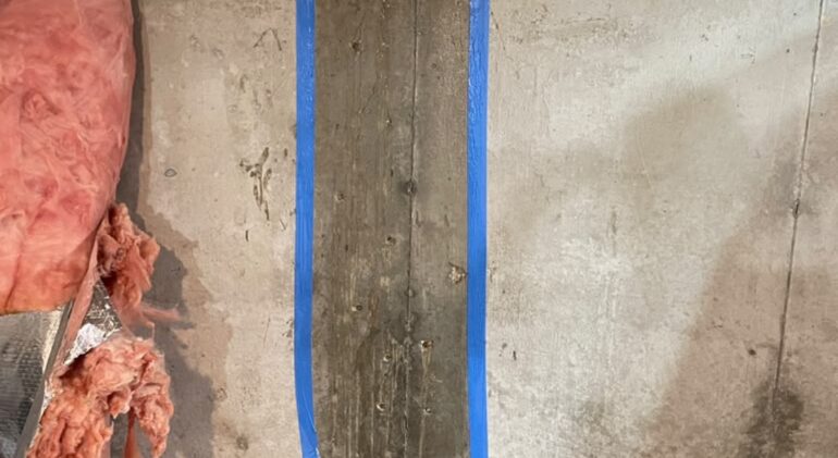 Poured concrete foundation wall with blue tape marking the working channel along the length of a crack before injection begins