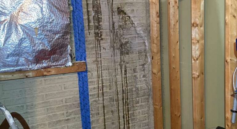 Heavy rust-coloured water staining running down a foundation wall from a leaking crack, with blue tape marking the repair area