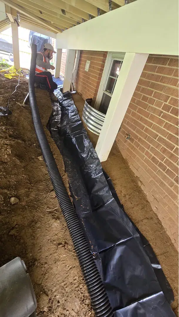 Near-grade grading tile with sloped sheet and perforated drain pipe beside a Kensington foundation