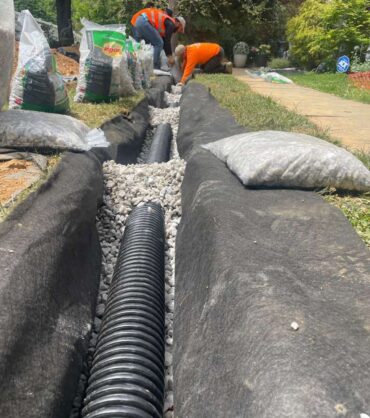Perforated corrugated drain pipe laid in washed gravel inside a trench lined with non-woven geotextile fabric