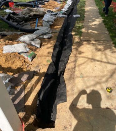 Open drainage trench lined along both sides with black non-woven geotextile filter fabric before gravel is placed