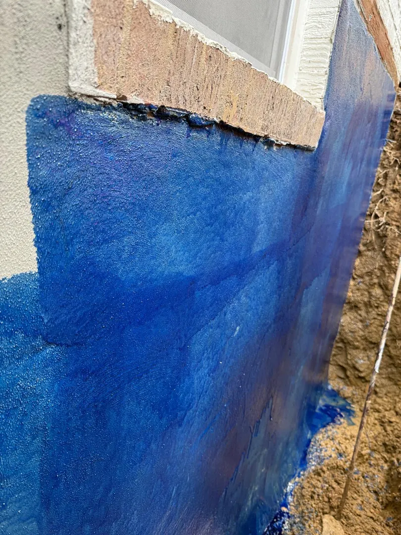 Bethesda, MD Foundation Leak: Exterior Waterproofing and Grading Tile 2 Blue primer on the exterior foundation wall below a basement window
