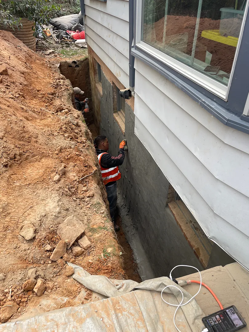 Exterior Waterproofing in Rockville, MD: Windowed Foundation Wall Case 5 Crew applying gray cementitious waterproofing coat to an excavated foundation wall in Rockville